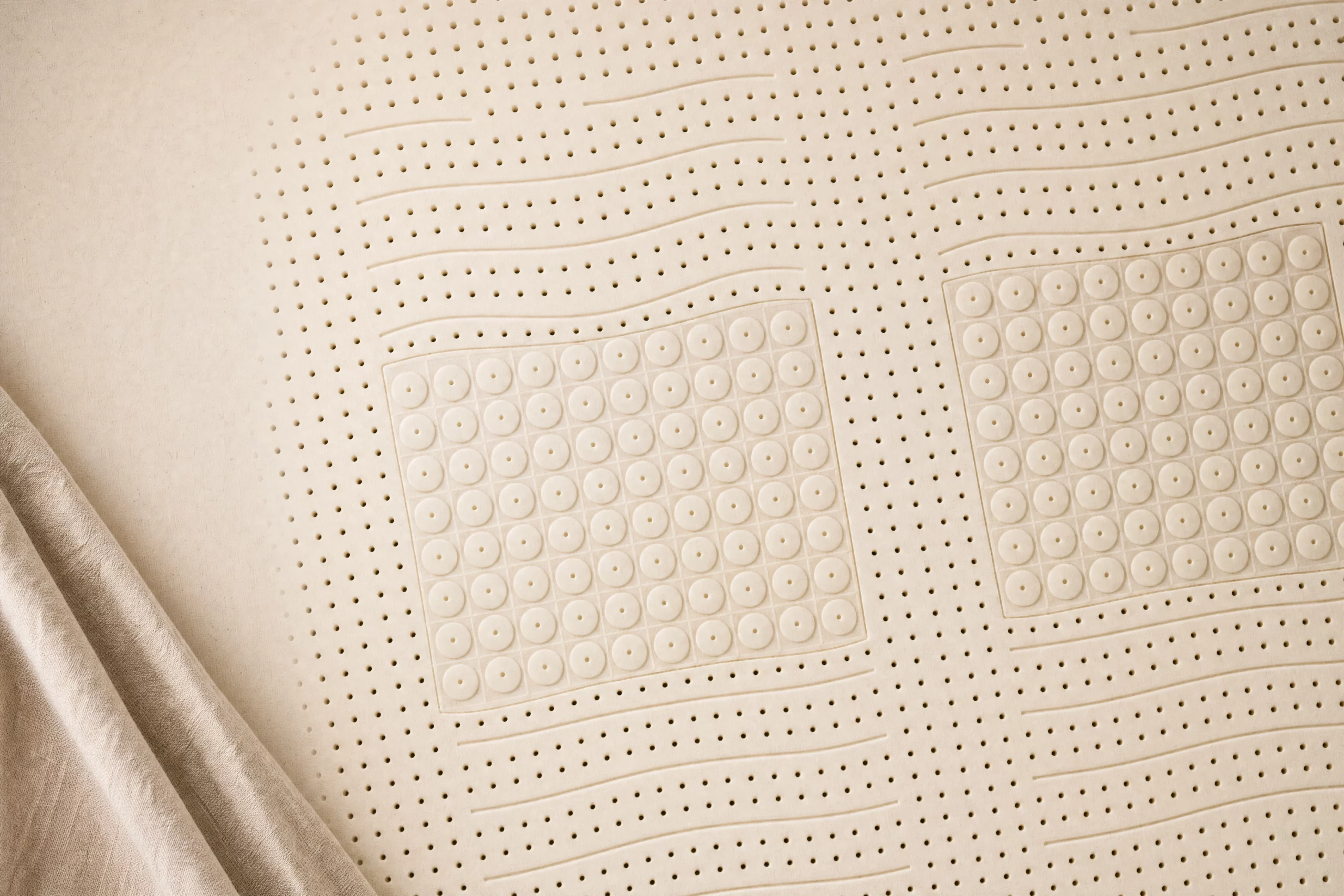Superficie cenital de un colchón de látex 100% natural con perforaciones de ventilación y zonas de firmeza, en tono beige natural